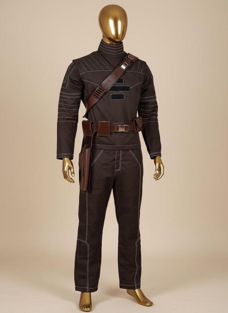 May include: A dark brown long-sleeved shirt and matching trousers set featuring white contrast stitching, a high collar, and a brown utility belt with a holster. The outfit includes a brown shoulder strap with metallic accents and black rectangular patches.