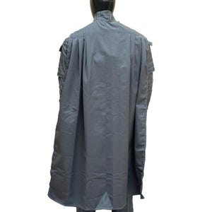 May include: A gray, long coat with a high collar and cape-like design. The coat is displayed on a mannequin, showcasing its tailored fit and structured silhouette. The fabric appears to be a medium-weight material.