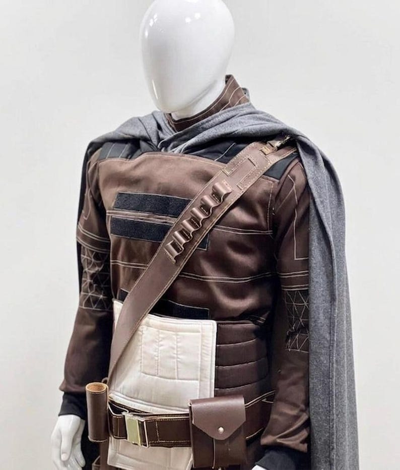 May include: A brown and black costume displayed on a mannequin. The outfit features a long-sleeved top with black detailing, a utility belt with pouches, and a grey cape. The costume has a futuristic or fantasy theme.
