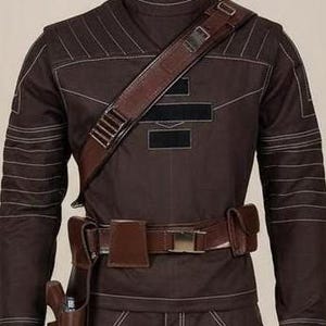 May include: A dark brown long-sleeve jacket featuring a high collar, white contrast stitching, and a diagonal brown leather shoulder strap with metal hardware. A matching brown leather utility belt with pouches and a holster is worn at the waist.