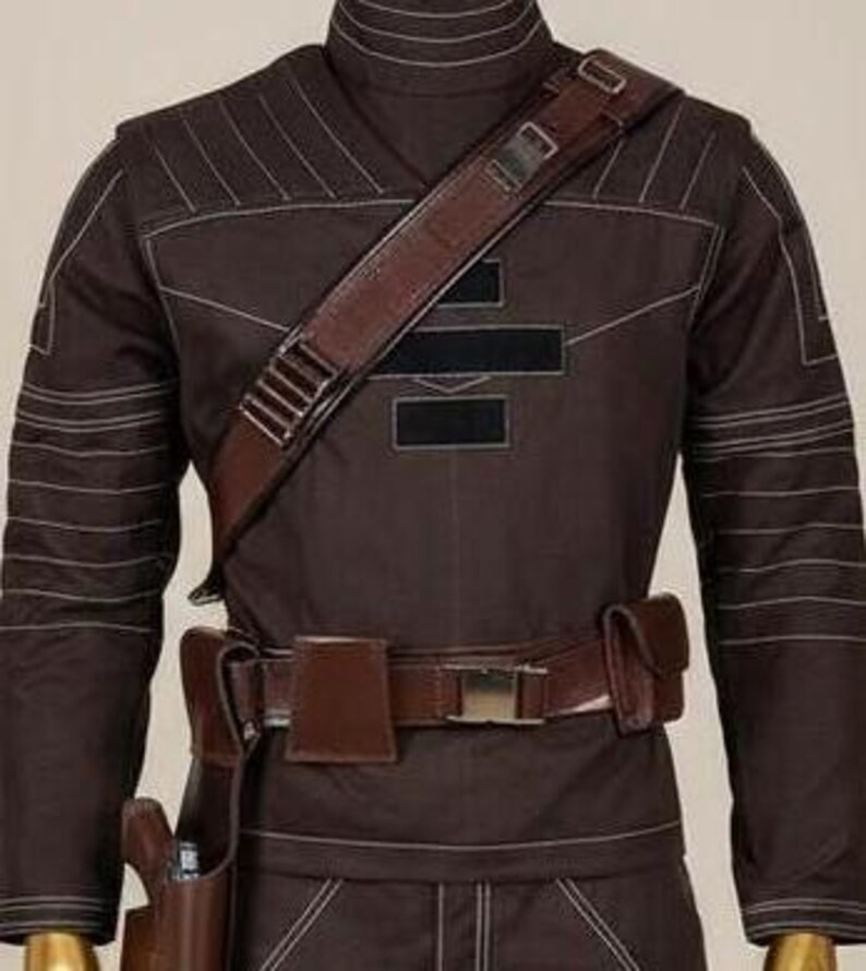 May include: A dark brown long-sleeve jacket featuring a high collar, white contrast stitching, and a diagonal brown leather shoulder strap with metal hardware. A matching brown leather utility belt with pouches and a holster is worn at the waist.