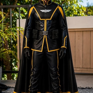 May include: A black leather-style costume featuring yellow trim, a high collar, and a matching cape. The jacket includes a silver winged emblem on the chest, a utility belt with two attached pouches, and long sleeves. Black trousers and boots complete the set.