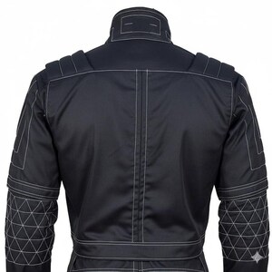 May include: A black jacket featuring a high collar, structured shoulder panels, and long sleeves with a white triangular grid pattern on the lower arms. The garment is accented with prominent white topstitching along the seams and back panel.