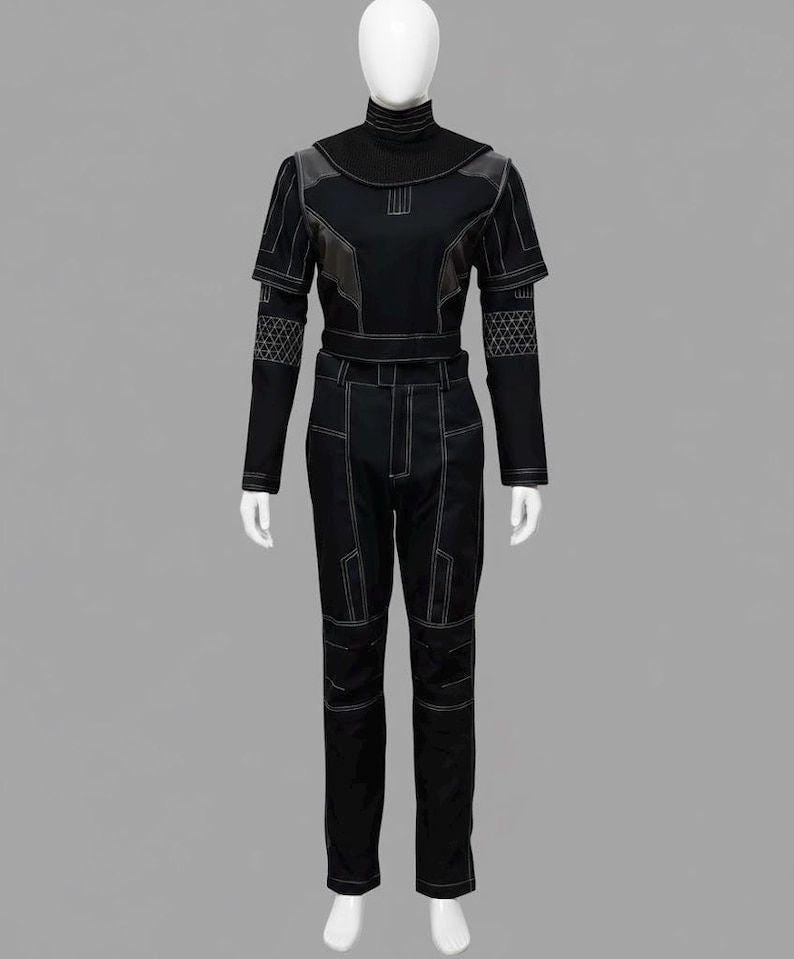 Peut inclure: Un costume noir pr&eacute;sent&eacute; sur un mannequin. La tenue comprend un haut &agrave; col montant avec des accents g&eacute;om&eacute;triques et des coutures blanches, associ&eacute; &agrave; un pantalon assorti. Le costume a un design futuriste.