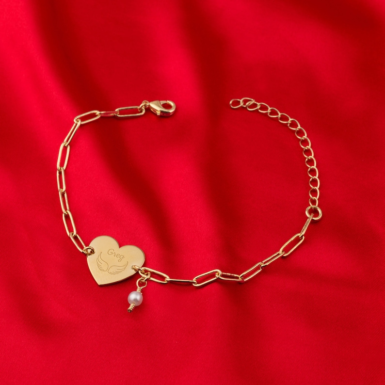 a gold bracelet with a heart and a pearl