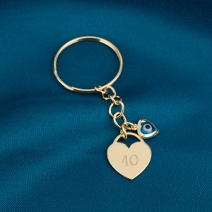 May include: Gold-tone keychain with a heart-shaped charm engraved with the number "10" and a smaller charm with a blue evil eye design.