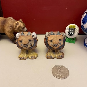 May include: Two ceramic lion figurines with brown bodies, yellow feet, and spiky manes. A brown bear figurine and a sheep figurine are also visible. A coin is in the foreground.