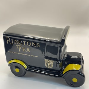 Peut inclure: Un pot à thé en céramique noire en forme de camionnette de livraison vintage avec des accents jaunes sur les passages de roue. Le côté présente un texte doré RINGTONS TEA DOOR TO DOOR DELIVERY SERVICE SINCE 1907 et un logo écusson doré.