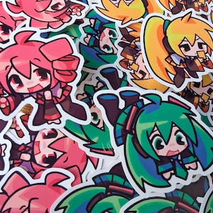 May include: A collection of colorful anime-style stickers featuring various characters with large eyes and expressive faces. The stickers showcase a variety of vibrant colors, including pink, green, and yellow, with black outlines.