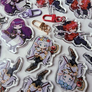 May include: A selection of clear acrylic charms depicting anime-style characters. The charms display diverse characters with intricate designs, including those with long hair, weapons, and floral details. Several keychains in gold, red, and purple are also visible.