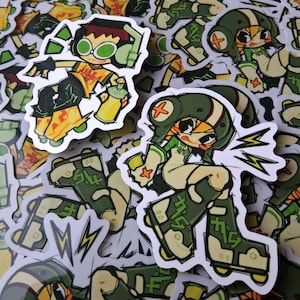 Op de afbeelding: Een verzameling cartoonstickers met personages in actieposes. De stickers tonen personages met groene brillen, helmen en rolschaatsen, die spuitbussen vasthouden en bliksemschichten tonen. Het kleurenpalet omvat groen, geel en zwart.