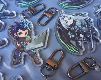 May include: Clear acrylic keychains featuring chibi-style anime characters. One character has spiky dark hair and holds a large sword, while another has long silver hair, black wings, and a katana. Each keychain includes a dark metal lobster clasp.