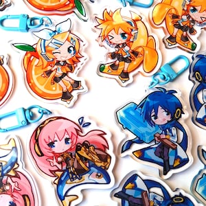 May include: A selection of colourful acrylic charms featuring anime-style characters. The charms depict characters with vibrant hair and outfits, set against fruit-themed backgrounds like oranges and bananas. Each charm includes a blue clasp for attachment.