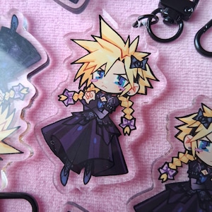 May include: Clear acrylic charm depicting a cartoon character with spiky blonde hair, blue eyes, and a black dress with purple accents. The charm has a black keychain attachment. Other charms are visible.