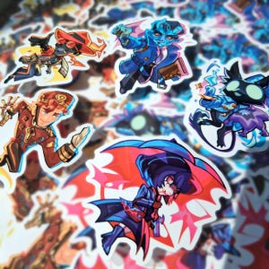 Op de afbeelding: Een verzameling gestanste vinylstickers met diverse gestileerde stripfiguren in dynamische houdingen. De ontwerpen bevatten figuren in blauwe, rode en oranje outfits, met levendige kleurenpaletten, scherpe omlijningen en expressieve gelaatstrekken.