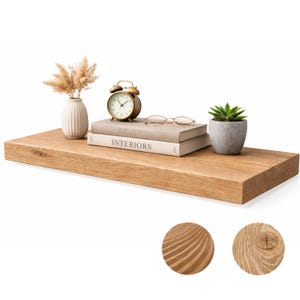 May include: A rectangular, light brown wooden shelf with a natural wood grain. The shelf holds a small vase with dried flowers, a gold alarm clock, two books, a small succulent in a gray pot, and a pair of glasses. Two wood samples are at the bottom.