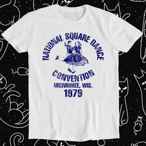 May include: White t-shirt with a blue vintage graphic of a couple square dancing. The graphic says "National Square Dance Convention Milwaukee, Wis. 1979".