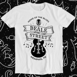 Pode incluir: Camiseta branca com um design gráfico preto e branco com um violão e o texto "Home of the Blues Beale Street Memphis, TN".