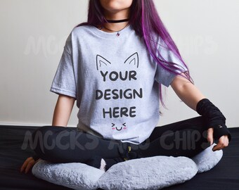 May include: A gray t-shirt with the text "YOUR DESIGN HERE" and a pair of cat ears above the text. The shirt has a cute smiley face below the text. The t-shirt is being worn by a person with purple hair.