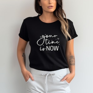 K&ouml;nnte beinhalten: Schwarzes T-Shirt mit dem wei&szlig;en Text "your time is NOW" in Schreibschrift. Das Shirt hat kurze &Auml;rmel und einen Rundhalsausschnitt. Das Model tr&auml;gt eine graue Jogginghose.