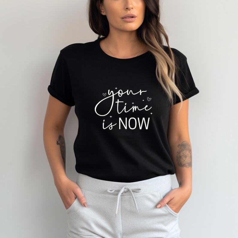 K&ouml;nnte beinhalten: Schwarzes T-Shirt mit dem wei&szlig;en Text "your time is NOW" in Schreibschrift. Das Shirt hat kurze &Auml;rmel und einen Rundhalsausschnitt. Das Model tr&auml;gt eine graue Jogginghose.
