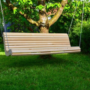 May include: A wooden swing bench suspended from chains, hanging from a tree branch. The bench is made of light-colored wood with horizontal slats. The background features green grass and foliage, creating a natural outdoor setting.