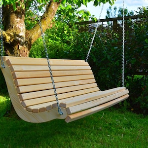May include: A wooden swing bench suspended from a tree by metal chains. The swing has a curved back and seat made of horizontal wooden slats. The surrounding area features green grass and foliage, creating a natural outdoor setting.