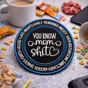 May include: A round, black patch with the text "YOU KNOW mom shit" in white script, surrounded by a blue border. The border text reads "DIRTY HOUSE - LATE NIGHTS - EARLY MORNINGS - MESSY HAIR - BATHROOM - SANCTUARY - HIDDEN SNACKS".