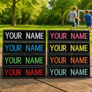 May include: Black rectangular patches with the text "YOUR NAME" embroidered in various colors, including white, pink, blue, green, yellow, orange, and red. The patches are stacked on a wooden surface, with a green grassy background.
