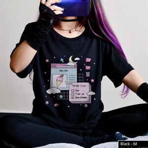 May include: Black t-shirt featuring a graphic of a computer screen with a recipe and a to-do list. The graphic includes a pink ice cream cone, a moon, and stars. The text on the shirt reads "Recipe" and "TO-DO list".