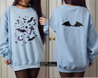 May include: Light blue sweatshirt with a black bat and purple stars design on the front and a single black bat on the back. The text "Light Blue - S" and "Model - 4'9"/146cm" is printed on the bottom of the sweatshirt.