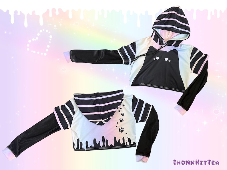 May include: Black and white cropped hoodie with a cat face design on the front. The sleeves are black with white accents, and the hood features black and white stripes. The back of the hoodie has paw prints and dripping paint details.
