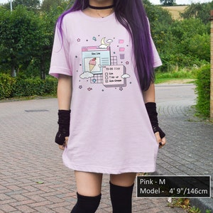 May include: An oversized pink t-shirt featuring a graphic of a computer screen with a to-do list that reads "Gm, Tidy up, Ice-Cream". The model is wearing the shirt in size M and is 146 cm tall.