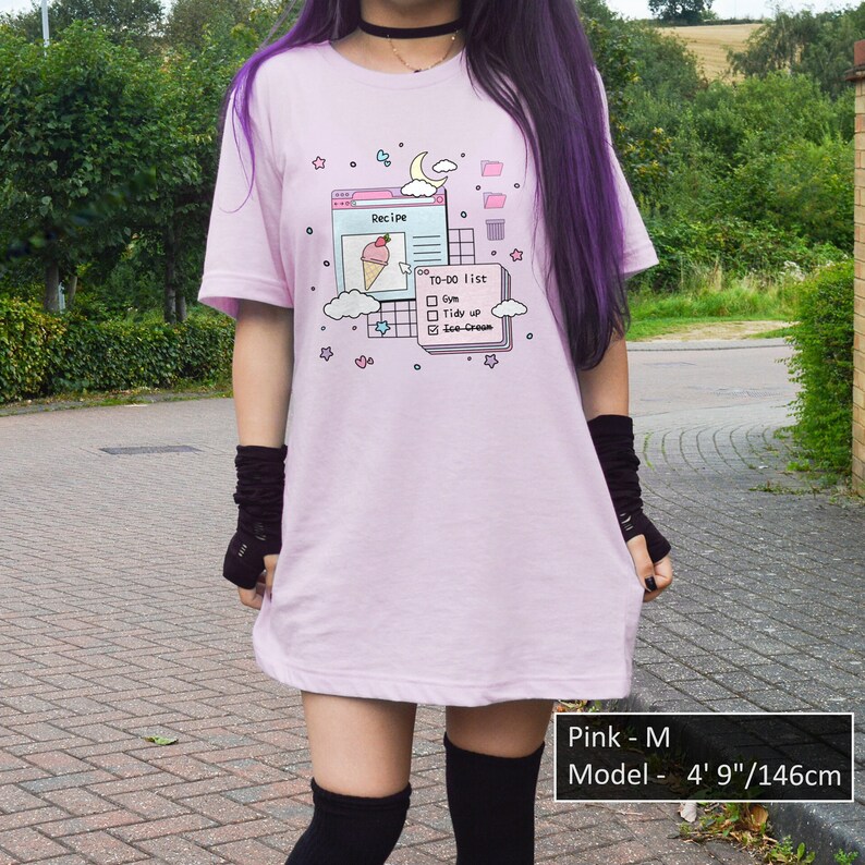 May include: An oversized pink t-shirt featuring a graphic of a computer screen with a to-do list that reads "Gm, Tidy up, Ice-Cream". The model is wearing the shirt in size M and is 146 cm tall.