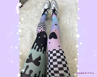 May include: Leggings featuring a mismatched pattern of black and white checkerboard, pastel blue and pink melting drip designs, black bows, and small stars. The leggings are paired with white lace-up shoes with black trim and a checkerboard pattern on the toe.