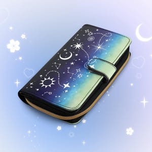 May include: A celestial-themed wallet with a zipper closure and a snap closure. The wallet features a design of stars, moons, and suns against a gradient background of blue and green. The zipper is gold-colored.