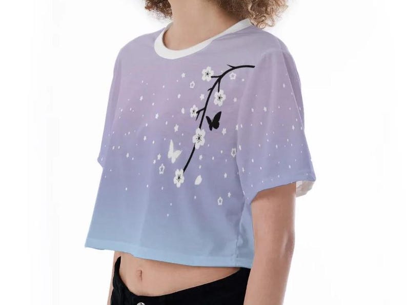 May include: A light blue and purple ombre crop top with a white floral design and black butterflies. The top has short sleeves and a round neckline.