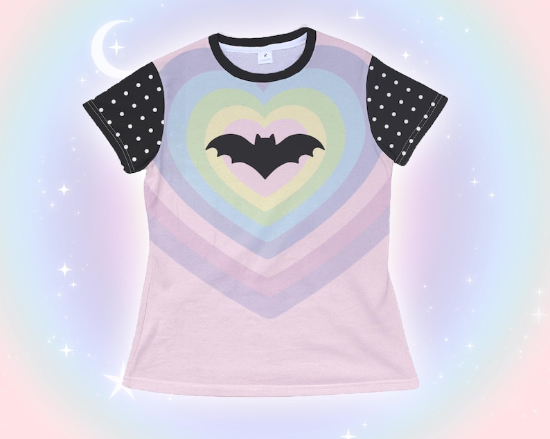 May include: A light pink t-shirt featuring a rainbow heart design with a black bat silhouette in the center. The sleeves are black with white polka dots, and the neckline is black.