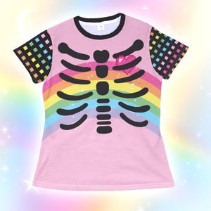 Op de afbeelding: Roze t-shirt met een zwart ribbenkastontwerp over een regenboog. De shirt heeft een zwarte kraag en mouwen met een kleurrijk geruit patroon. Een gepixeld roze hart bevindt zich boven de ribbenkast.