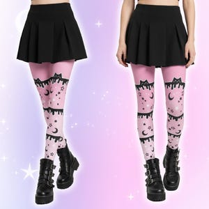 Może przedstawiać: R&oacute;żowe legginsy z wzorem czarnych kot&oacute;w, księżyc&oacute;w i gwiazd. Legginsy mają czarny, ociekający wz&oacute;r na g&oacute;rze. Modelka ma na sobie czarną plisowaną sp&oacute;dnicę i czarne buty.