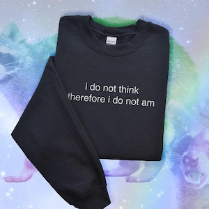 May include: Black crewneck sweatshirt with the text "i do not think therefore i do not am" in white. The sweatshirt is displayed against a colorful background with raccoon illustrations.