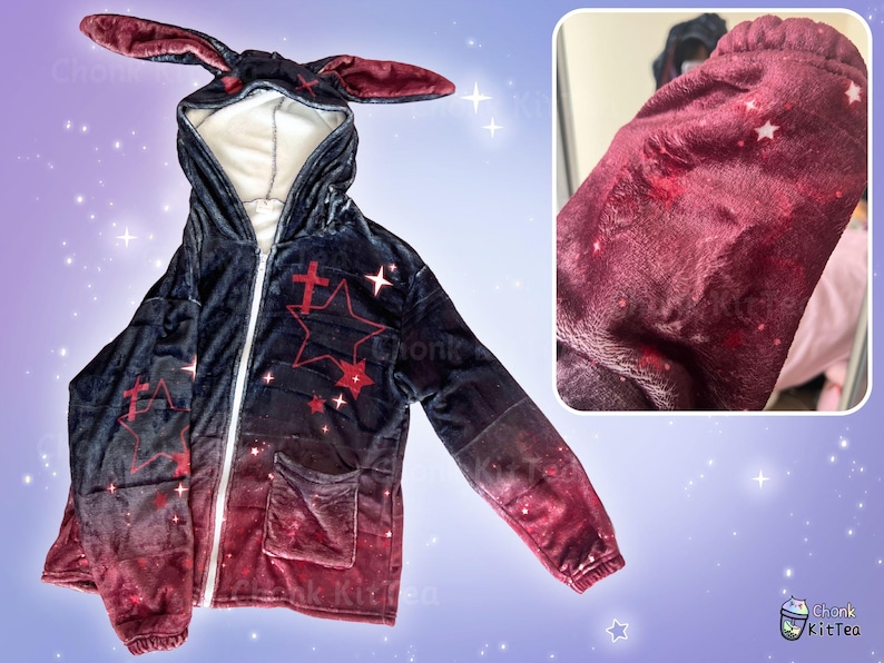 May include: A black and red hooded sweatshirt with a gradient design featuring stars and crosses. The hoodie has bunny ears attached to the hood.