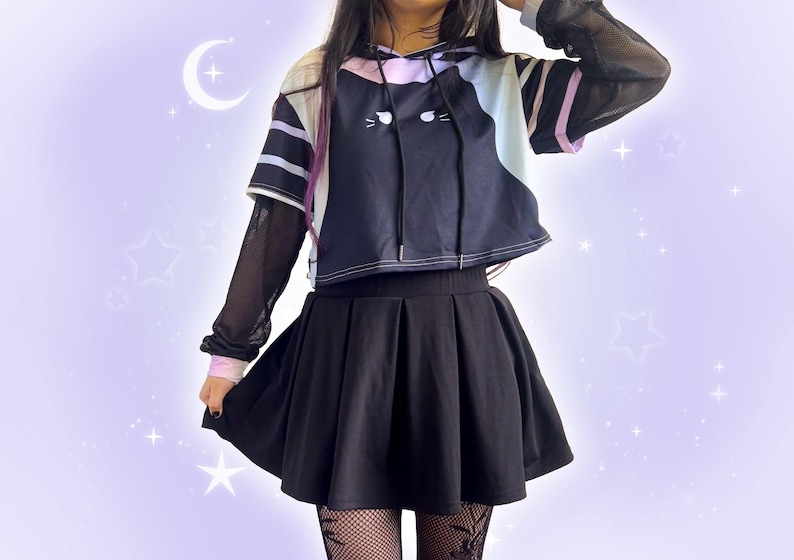 May include: A black pleated skirt paired with a black and white cat-themed hoodie. The hoodie has a cat face design and is layered over a sheer black long-sleeved shirt. The outfit is completed with fishnet stockings.