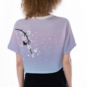 May include: A light blue and purple ombre crop top with a white floral design and black butterflies. The top has short sleeves and a round neckline.