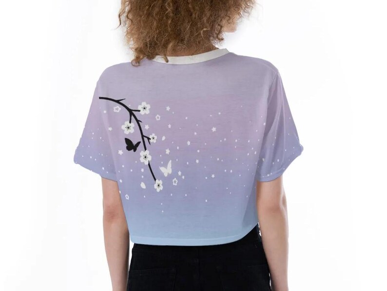 May include: A light blue and purple ombre crop top with a white floral design and black butterflies. The top has short sleeves and a round neckline.