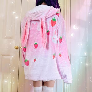a girl wearing a fluffy pink bunny hoodie with hanging bunny ears in the hood, cute strawberry milk themed