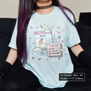 May include: A light blue t-shirt featuring a graphic of a computer screen with a recipe for ice cream and a to-do list. The graphic includes a pink ice cream cone with a strawberry on top, a pink check box list, and a pink folder icon. The text on the shirt reads "Recipe" and "To-Do List".