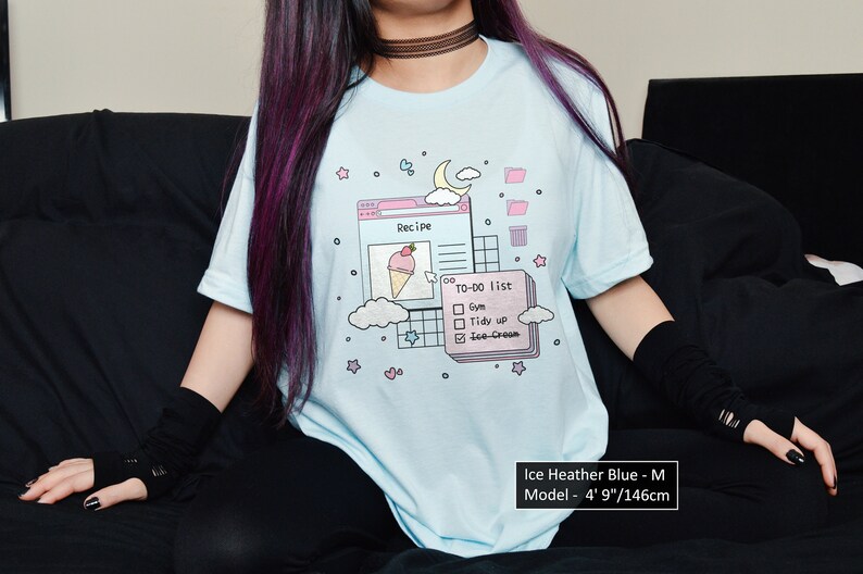 May include: A light blue t-shirt featuring a graphic of a computer screen with a recipe for ice cream and a to-do list. The graphic includes a pink ice cream cone with a strawberry on top, a pink check box list, and a pink folder icon. The text on the shirt reads "Recipe" and "To-Do List".