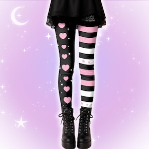 Op de afbeelding: Zwarte legging met een gesplitst ontwerp: de ene kant heeft roze harten en witte sterren op een zwarte achtergrond, de andere kant heeft roze en witte strepen. Gedragen met zwarte veterlaarzen.