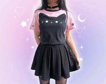 May include: A black and pink cat-themed t-shirt with a matching black pleated skirt. The t-shirt features a cat face design and paw prints on the sleeves. The outfit is a cute and stylish ensemble.